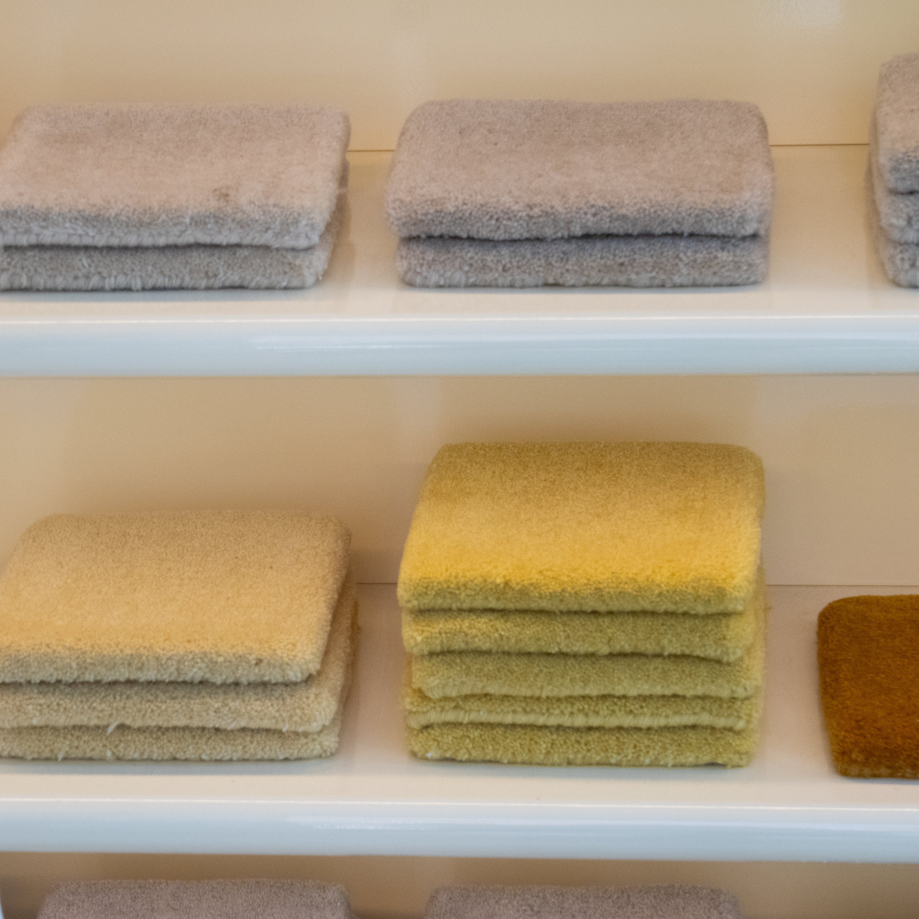Stacks of textured cushions in various colors on a white shelf.